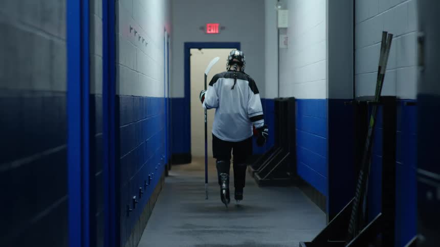 A hockey player grabs their stick and walks down the hall