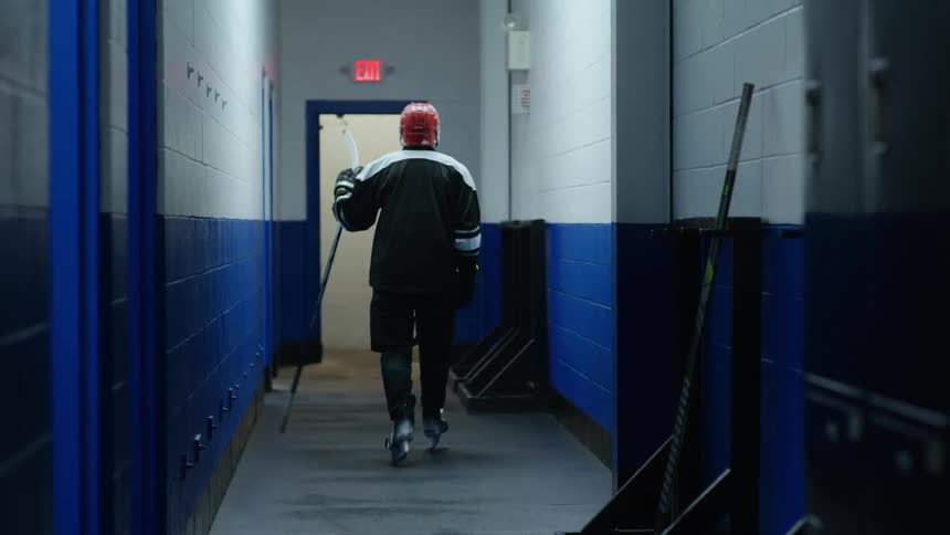 Hockey player picks up hockey stick and walks down hallway