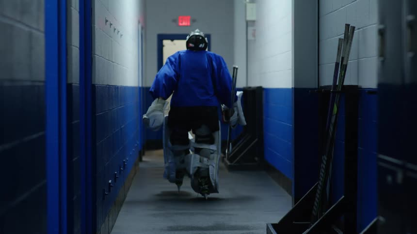 Goalie leaving the locker room and picking up his hockey stick