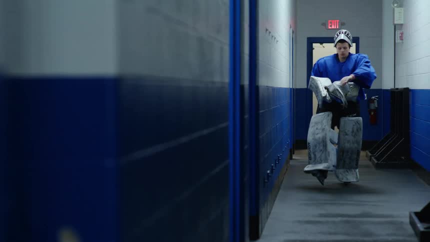A goalie walks down the hall and removes his helmet