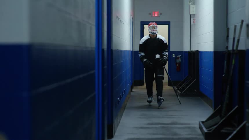Hockey player puts hockey stick in rack before entering room