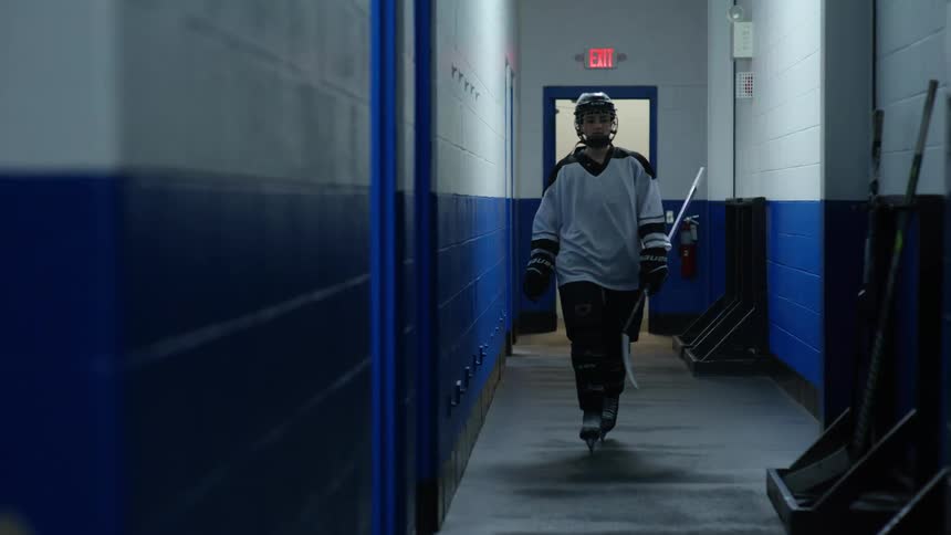Female player entering the hallway and placing her hockey stick on the wall