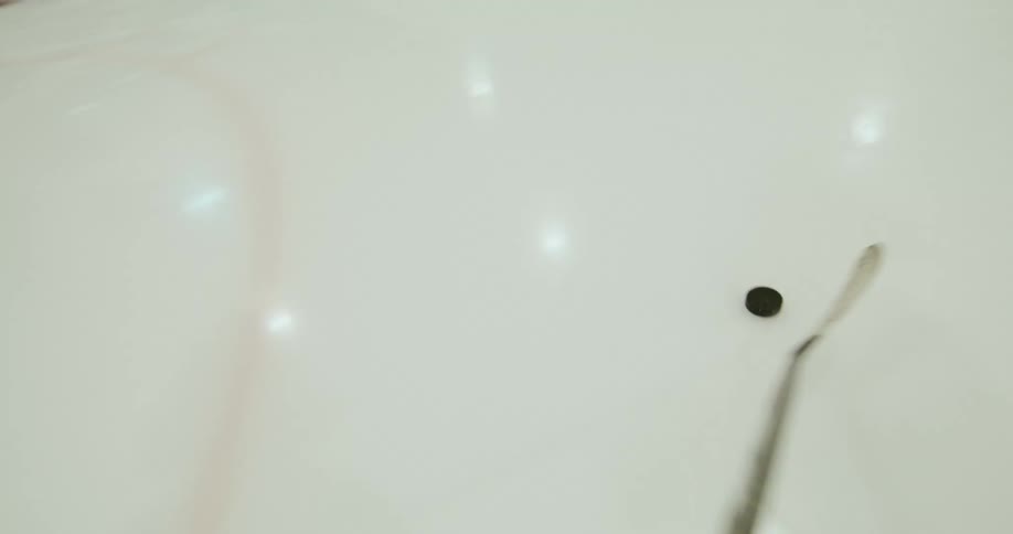Player point of view of a hockey stick driving the puck on a hockey rink