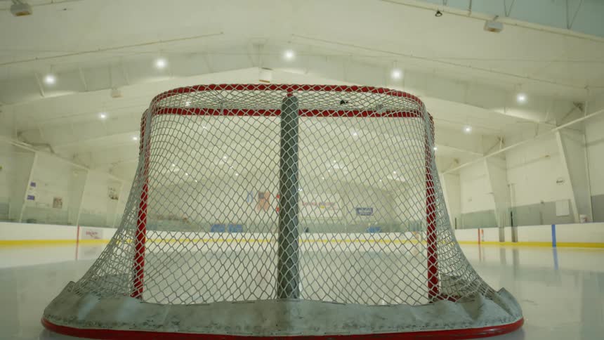 Ceiling lights come on in sections illuminating ice rink and hockey goal