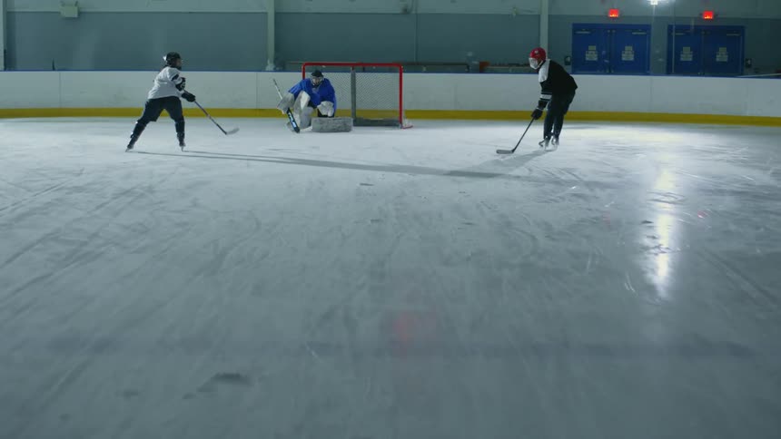 Two hockey players practicing shots on a goalie