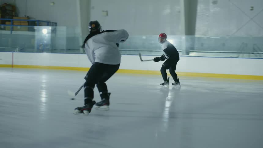 Two people are playing hockey on an ice rink and then score a point on a goal that a goalkeeper is defending