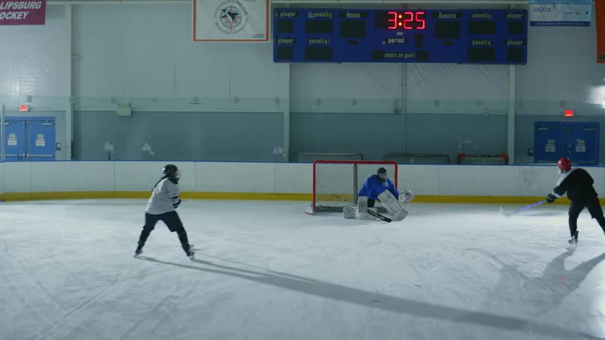 People playing hockey on an indoor ice rink with one of them acting as goalie and conceding a point