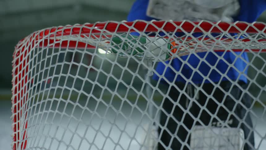 A person with hockey equipment and blue clothing is getting ready and is in front of the goal