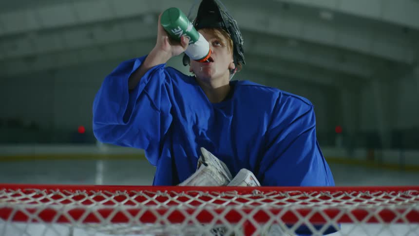 Man on a hockey court lifting a helmet and drinking water