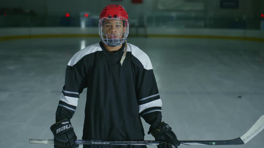 Hockey player pulls down helmet and stands holding hockey stick at an ice rink