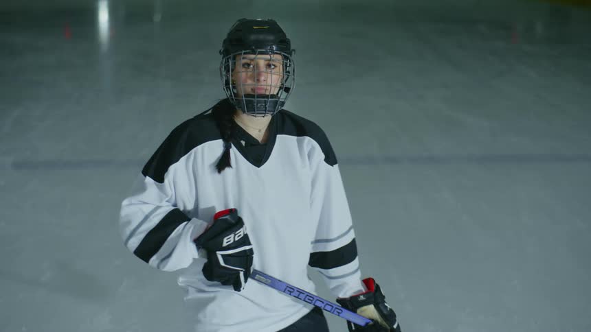 A female hockey player stands on an ice rink and looks at the camera