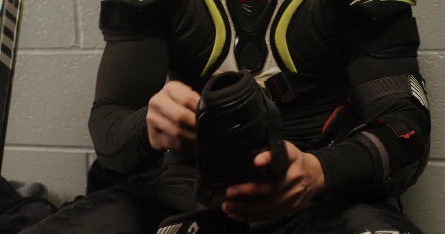 A hockey player is putting on his pads