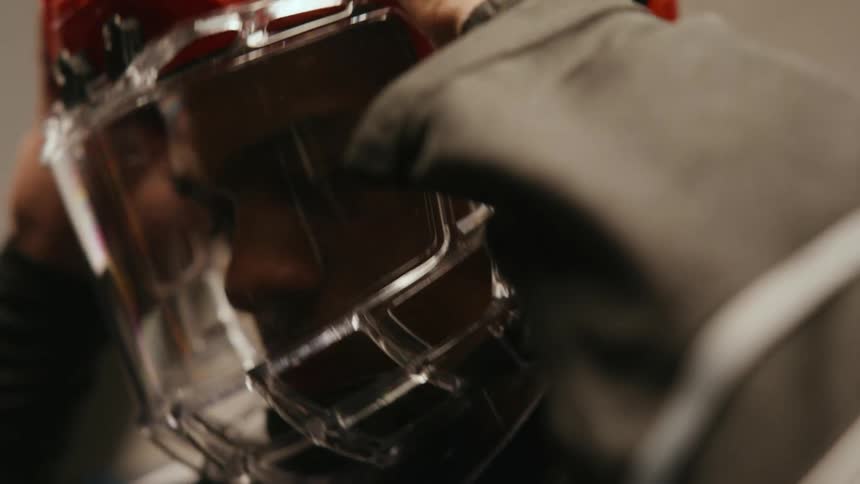 A hockey player adjusts his chin strap after securing his helmet and visor