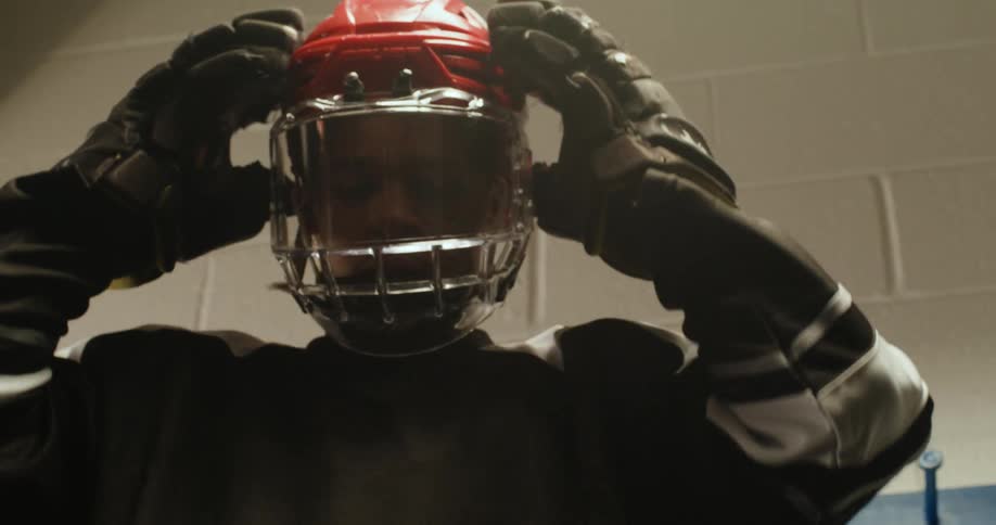 A hockey player wearing a black jersey puts on a red helmet