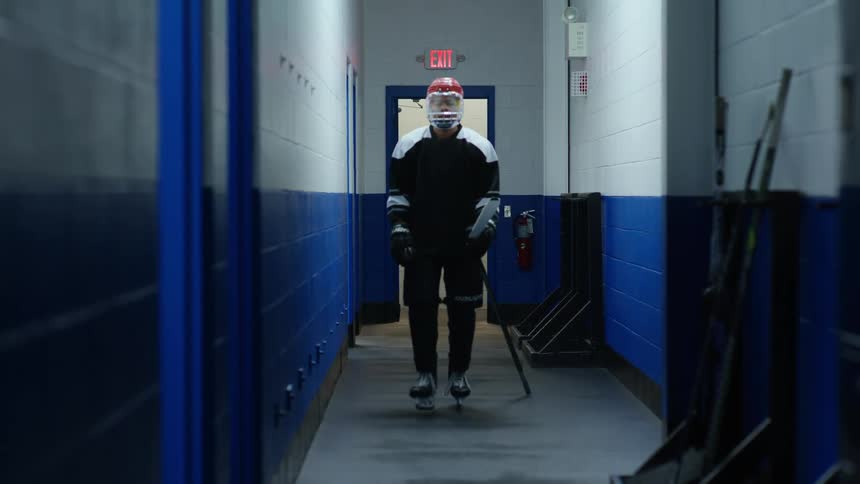 Male hockey player walks down corridor and puts away hockey stick before entering the locker room