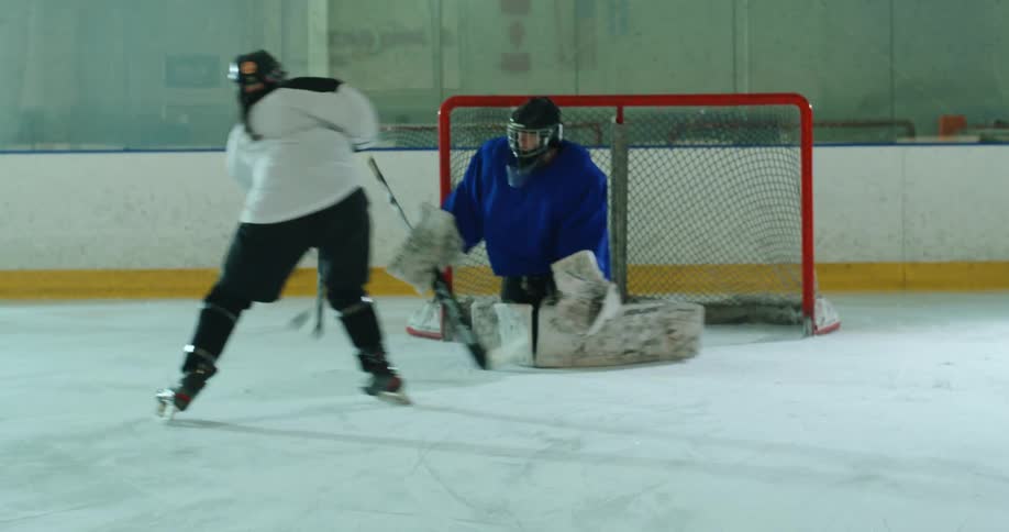 A hockey player skates away after taking a shot while the goalie extends their arm to block the puck