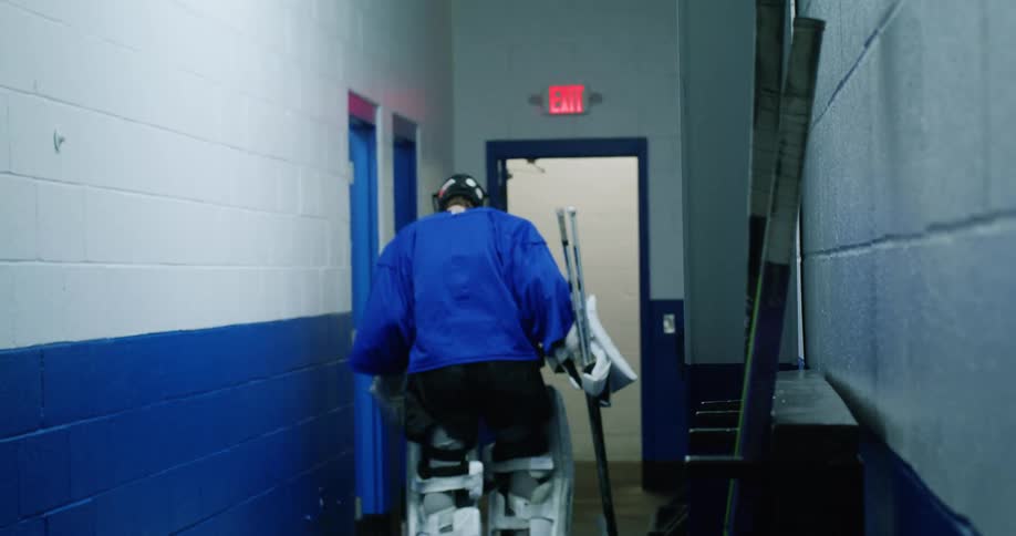 Man picking up a hockey stick and walking down the hallway