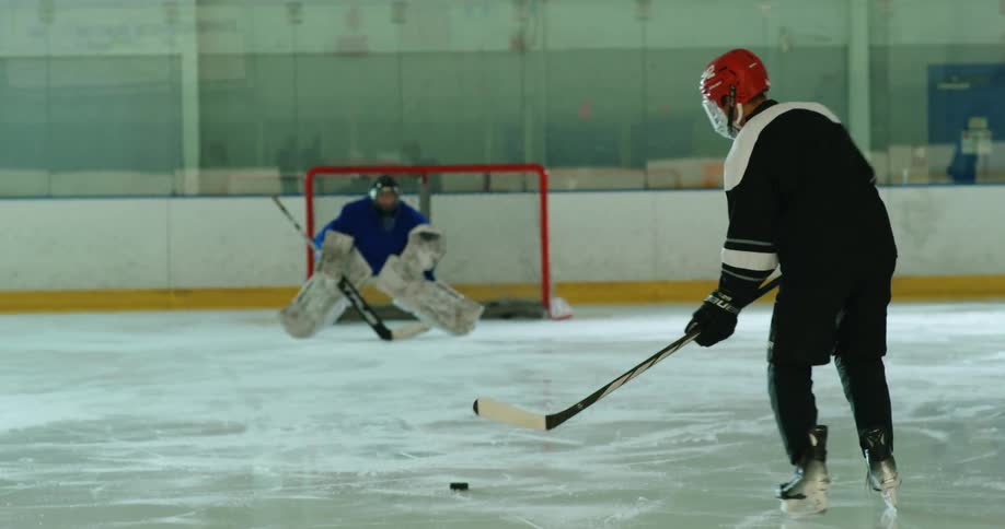 Player with a hockey stick throwing a puck towards the goalkeeper in practice