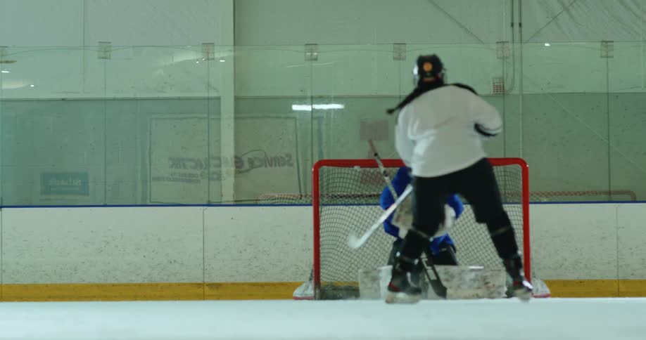Woman with a hockey stick throwing a puck towards the defending goalkeeper