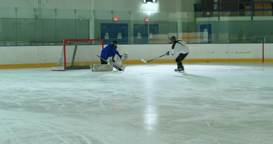 A hockey player attempts to shoot a puck into a net and a goalie stops it