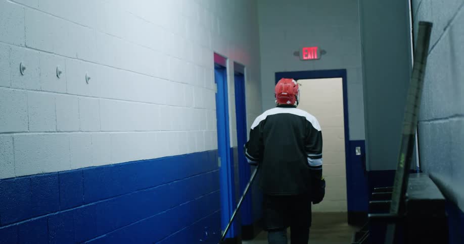 Young man picking up a hockey stick and walking down the hallway