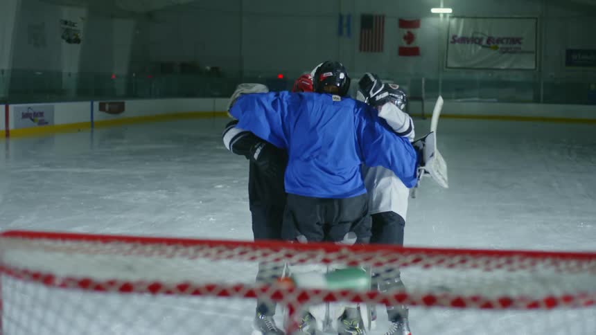 Three hockey playing friends hug on the ice of a dimly lit ice rink