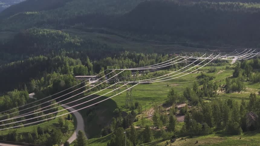 Power lines cross rural road near river leading past mountain to the city