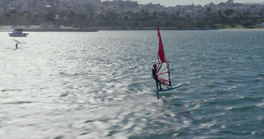 Aerial FPV of a man windsurfing along the coast
