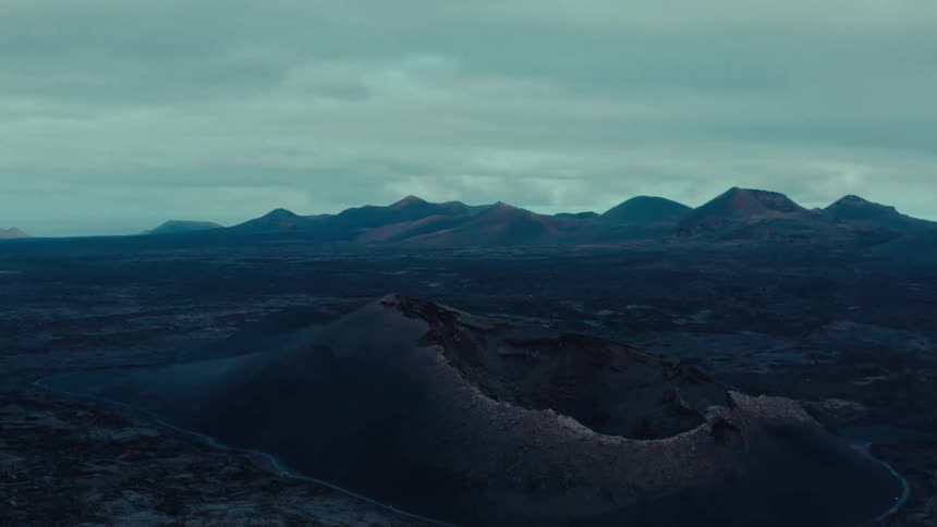A mountain with a volcanic crater sits near a mountain range