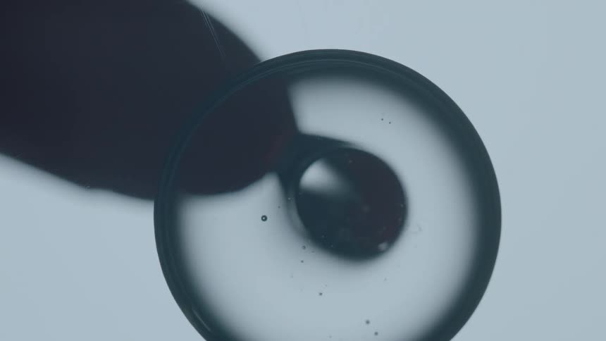 Dark liquid drop coming from a dropper onto a lens