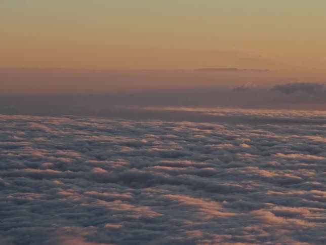 A view of clouds from an airplane windowthe clouds are puffy and white and the deep reddish sky fills most of the frame