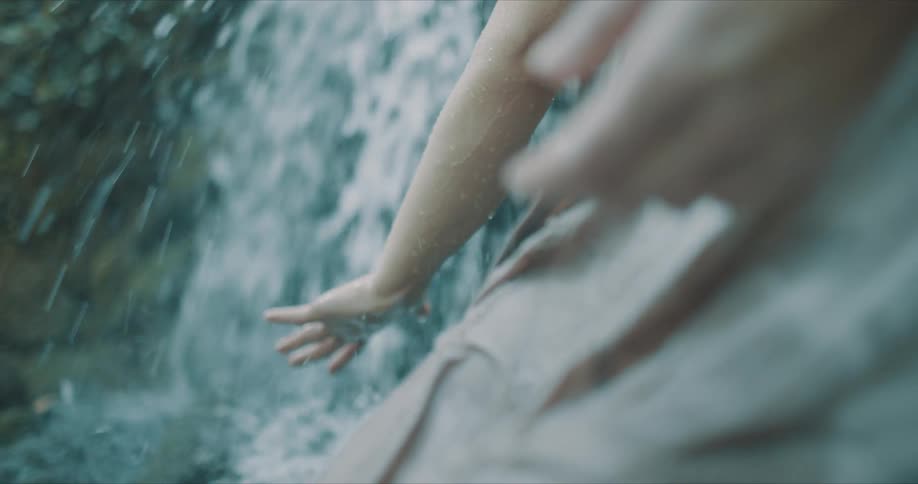 Woman holds her hand in the water flowing down a waterfall