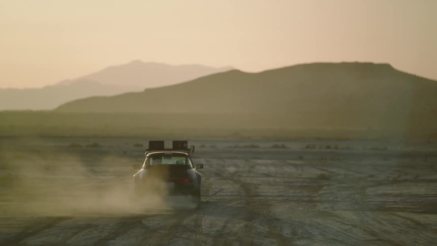 A car driving through a desert with a mountain range landscape in the background