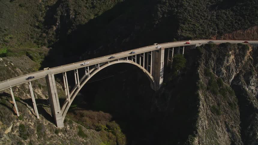 An aerial view of a large arched bridge spanning a deep canyon with vehicles traveling across it