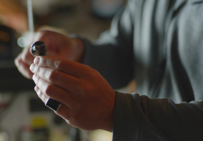 A bearded and bald man with tanned skin holds a piece of mechanica equipment and demonstrates how it works to his wife as she nods in affirmation.
