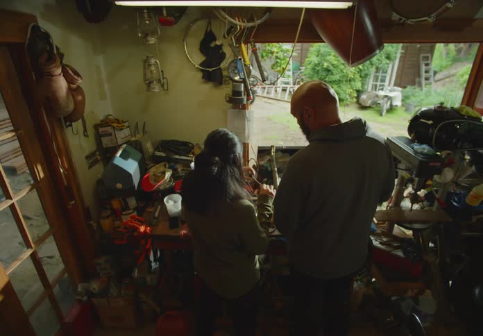 A man and a woman have a discussion over tools as they work on a hobby together in a cluttered workshop