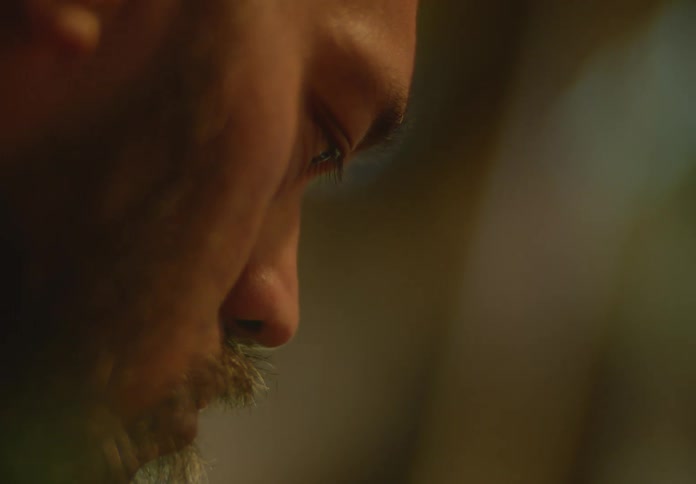 A bearded man-of-color is looking down intently at a project he is working on and muttering to himself while deep in thought.