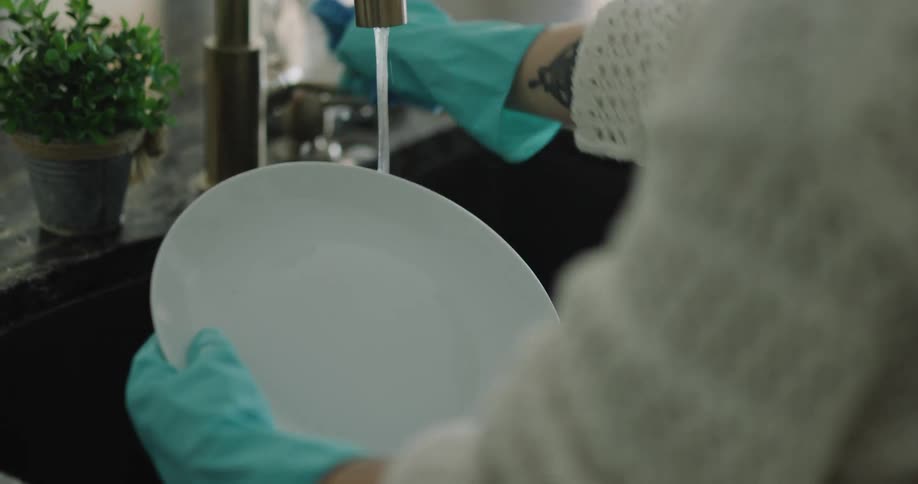 A woman rinses a plate in the sink in her kitchen