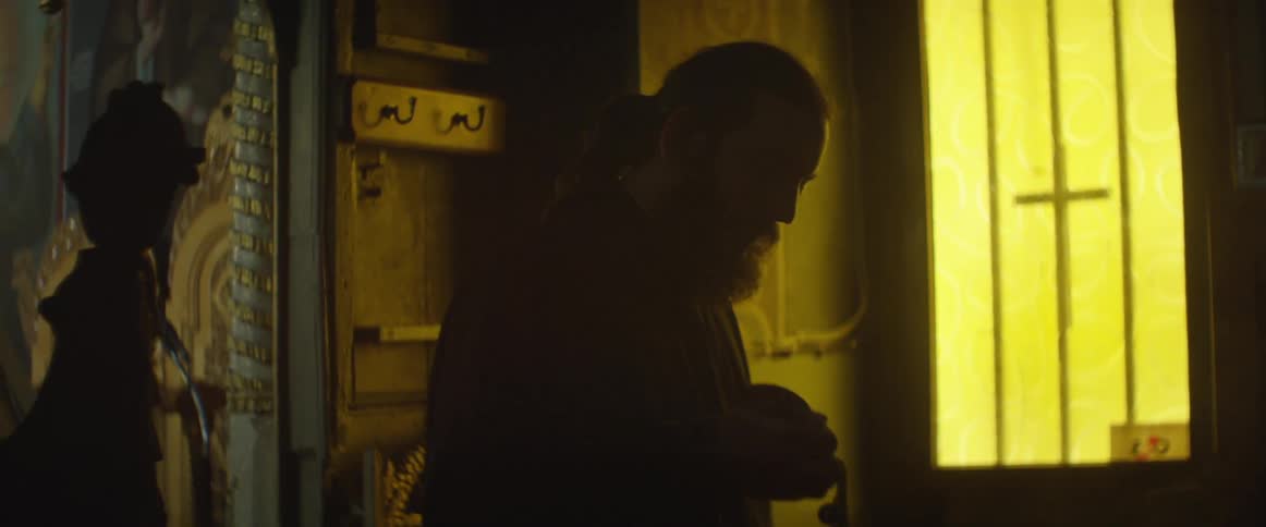 Bearded man with a ponytail dipping something repeatedly in a dark room