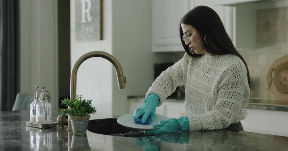 Woman wearing rubber gloves washing dishes at the kitchen sink