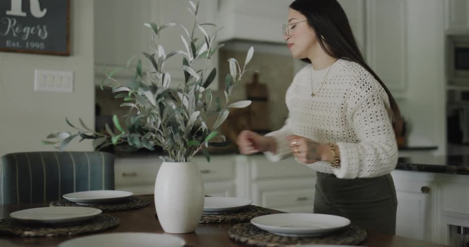 A woman places a vase on the dining table