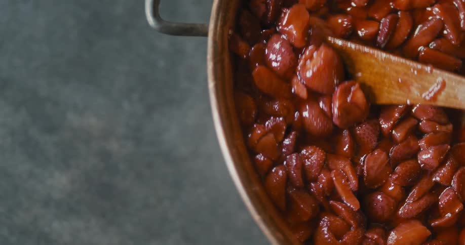 A person is mixing a pot full of strawberries