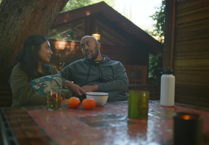 A couple cuddles at a table outside next to a cabin