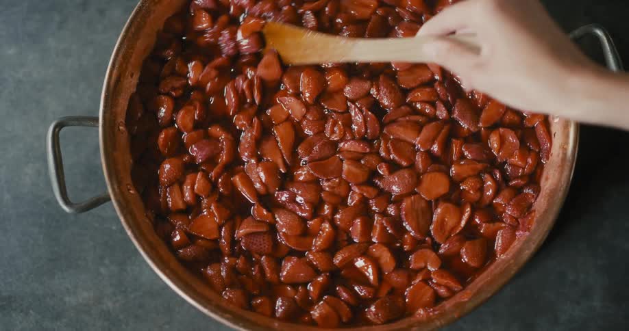 A person is stirring a pot full of strawberries