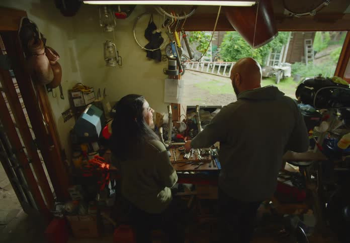 A man and woman talk and laugh together as they work on a hobby in their messy garage