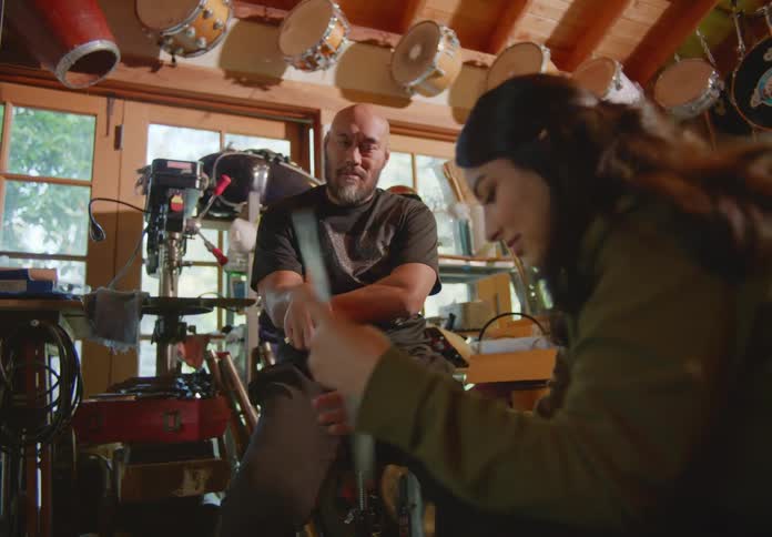 A man and woman sit in an outdoor storage shed going through some old things and she picks up a vinyl record while they chat back and forth about it.