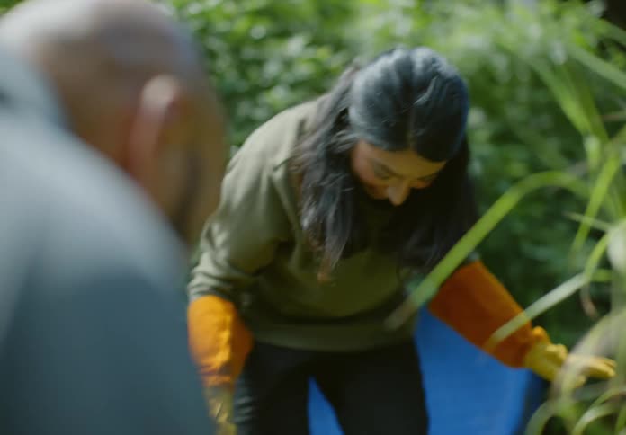 Man and woman crouching gardening outdoors next to grass