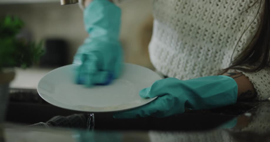 A woman scrubs a plate at a kitchen sink