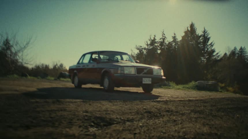 A car is parked on a flat dirt area near a forest