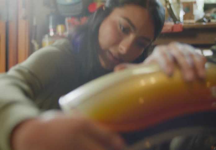 A young, ethnic woman is polishing and detailing a motorcycle wheel with a rag.